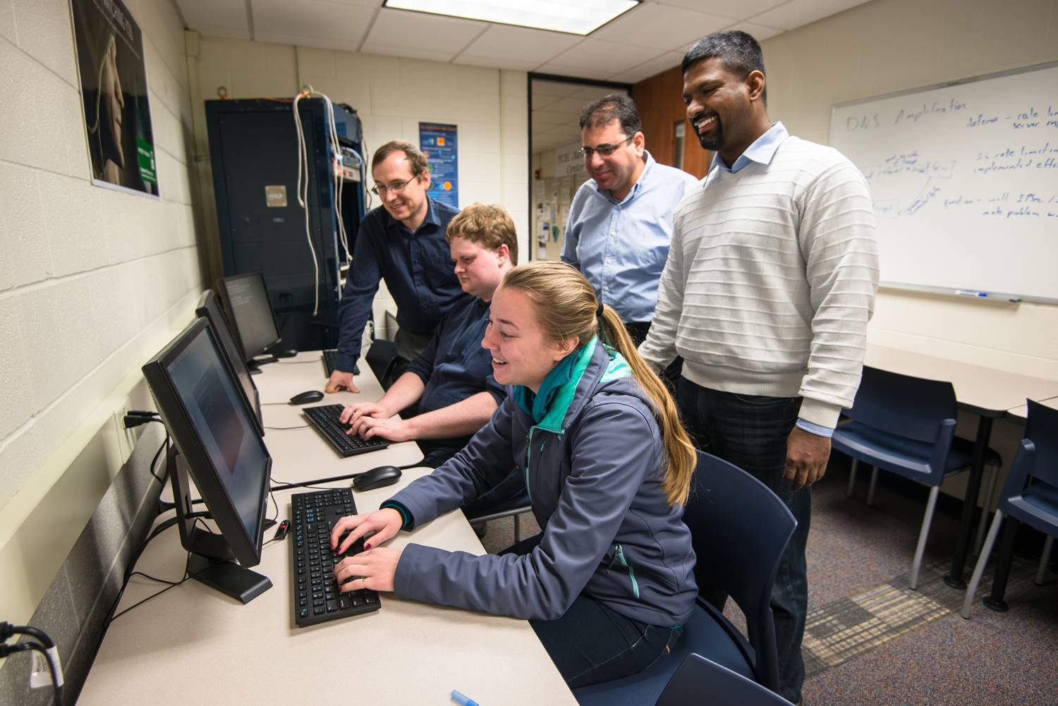 A group of faculty helping students in a research lab